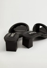 Czarne sandaly na blokowym obcasie z płaskim, zaokrąglonym wierzchem i bez pasków. Posiadają teksturowaną wkładkę i naszywkę z logo na górze.