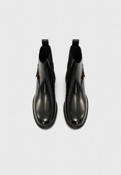 Černé kožené kotníkové boty s elastickými panely na stranách, kulatými špičkami a malými poutky. Hladká textura a minimalistický design.