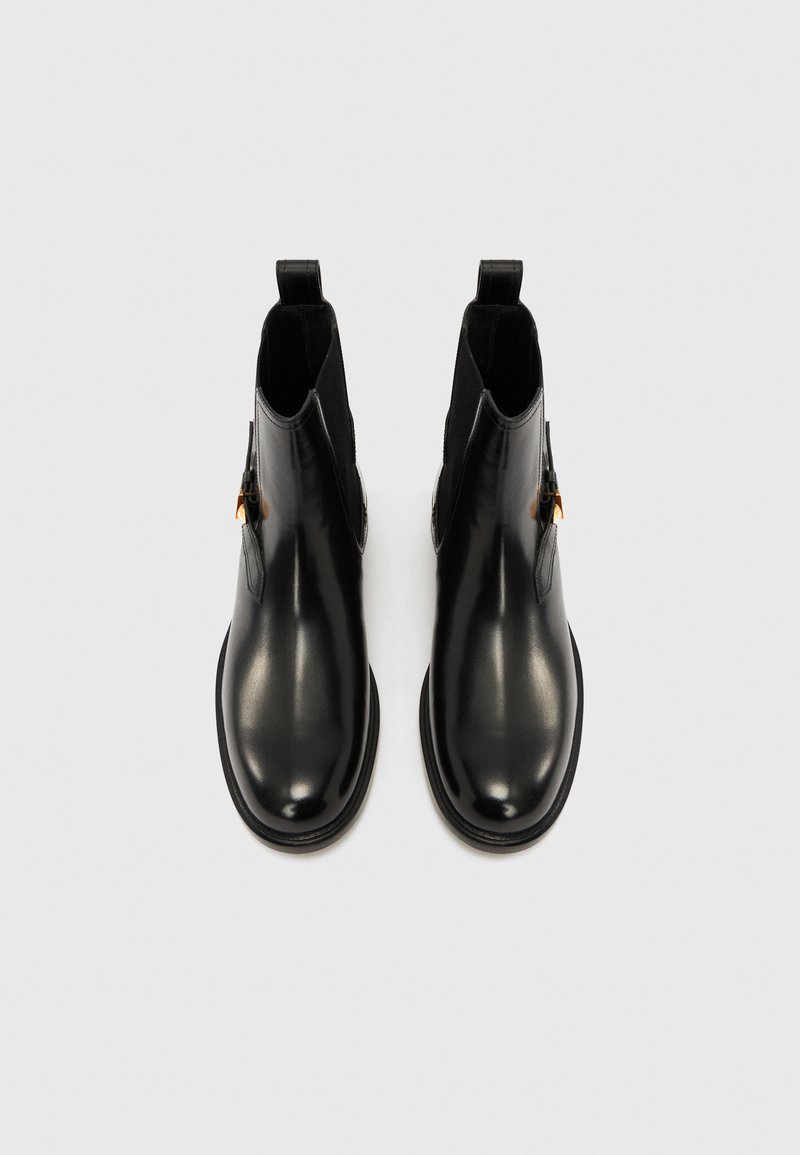 Svarte læderankelstøvler med elastiske paneler på siden, runde tæer og små trækflapper. Glat tekstur og minimalistisk design.