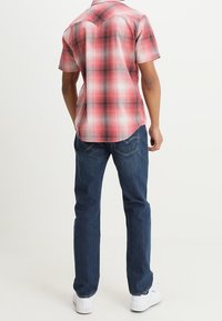 Koszula w kratę z krótkim rękawem w czerwono-białe kolory o strukturalnym kroju, zestawiona z niebieskimi dżinsami i białymi trampkami, prezentująca swobodny styl.