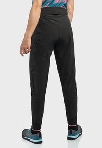 Schwarze Sporthose mit enganliegendem Schnitt, hohem Bund, Reißverschlusstaschen und strukturiertem Stoff. Mit einem Logo an der Seite akzentuiert.