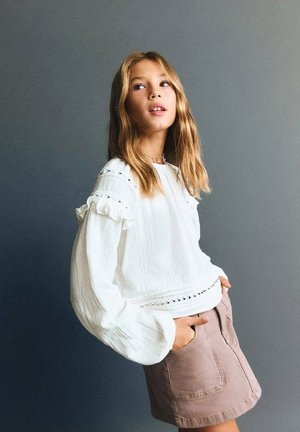 Witte, gestructureerde blouse met lange mouwen en ruches aan de mouwen, gecombineerd met een lichtbruine rok met zakken en een lichte A-lijn.