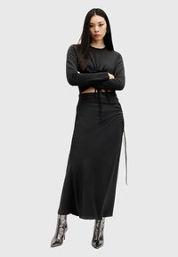 Zwarte lang mouwen crop top met gedraaide voorkant, gecombineerd met een bijpassende zwarte maxi rok met trekkoorden. Zilveren metallic enkellaarzen.