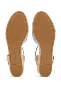 Paire de sandales compensées beige avec semelles en caoutchouc texturé et brides de cheville réglables, vues par le dessous, avec la marque Tommy Hilfiger.