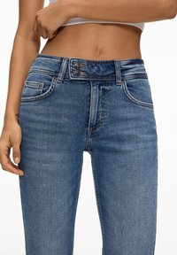 Modré džíny z denimu s středním pasem, s knoflíkovým zapínáním, pěti kapsami a mírně opotřebovanou texturou na látce.