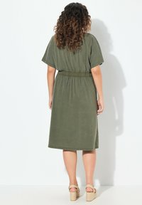 Oliwkowa midi sukienka z krótkimi rękawami, elastycznym pasem i luźnym krojem. Miękka tekstura, gładki wzór i zestawiona z sandałami na koturnie.