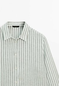 Chemise en lin avec des rayures verticales grises et blanches, col pointu, manches longues et patte de boutonnage. Texture légère et respirante.