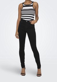Jeans skinny neri a vita alta abbinati a un top senza maniche a righe bianche e nere. I jeans presentano un classico design a cinque tasche.