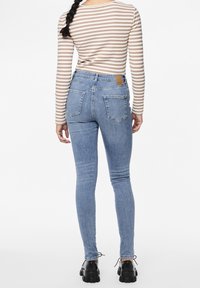 Högmidjade blå skinny jeans med en blekt tvätt, med två bakfickor och ett brunt läderlogo på midjan.