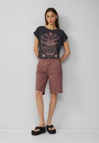 Zwart graphic T-shirt met korte mouwen, voorzien van een roze print; bordeauxrode shorts; zwarte platform sandalen; gladde stoffen; casual zomeroutfit.