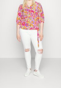 Haut floral en violet, rose et orange, avec des manches trois-quarts. Assortie à un jean blanc déchiré et des baskets blanches.