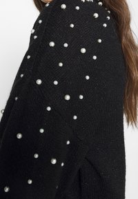 Maglione nero a maglia con tessuto testurizzato, arricchito da perle sparse su una spalla.