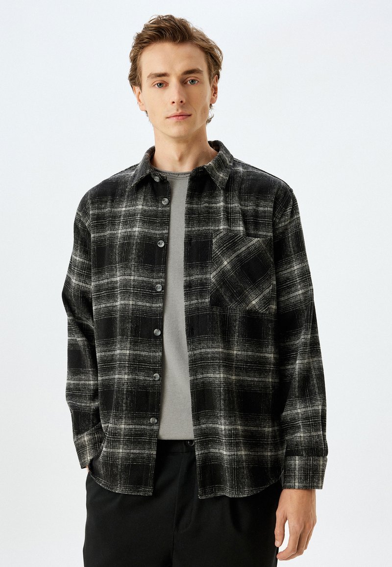 Camicia in flanella a quadri bianca e nera con bottone frontale, maniche lunghe, taschino singolo sul petto e strato interno grigio. Tessuto morbido.