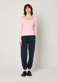 Maglione rosa a maniche lunghe con scollatura a V abbinato a pantaloni jogger blu navy, dotati di vita elastica e tasche laterali, completato da scarpe nere slip-on.