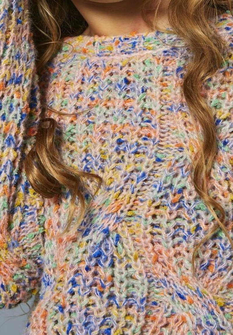 Gros plan d’un pull tricoté multicolore avec des nuances pastel et des motifs texturés, porté par une personne aux longs cheveux ondulés.