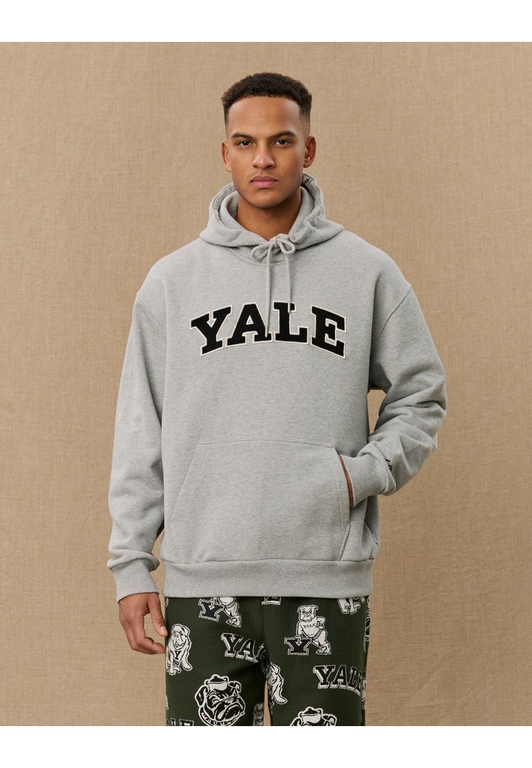 Gray hoodie featuring a large black "YALE" logo. It has a front pocket and drawstrings on the hood. Paired with green pants with printed designs.