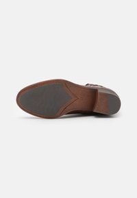 Semelle en cuir, marron avec une texture en caoutchouc noir pour une bonne adhérence et un léger talon. Présente une forme contournée avec des détails de couture subtils.