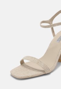 Beige haksandalen met een textuurstof bovenwerk, twee slanke enkelriemen, een vierkante neus en een blokhak met een gladde afwerking.