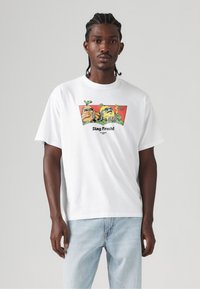 T-shirt bianca in cotone con una grafica colorata di personaggi dei cartoni animati, con il testo "Stay Fresh!" in grassetto nero sotto il disegno.
