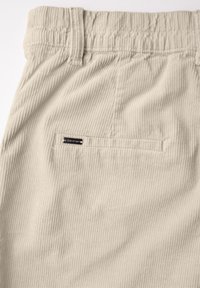 Lichtbeige corduroy stof met verticale ribbeling, met een elastische tailleband en een klein metalen label op de achterzak.