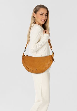 Borsa a spalla in pelle marrone con forma a mezzaluna, tracolla regolabile e dettagli di cucitura discreti, indossata in modo informale da un modello su uno sfondo semplice.