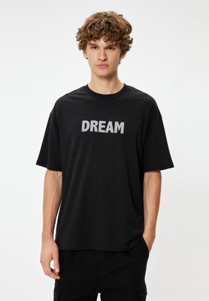 Sort bomulds t-shirt med et stort "DREAM" grafik i hvid på brystet. Korte ærmer og afslappet pasform med rund halsudskæring.