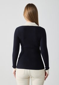 Navy ribbed knit sweater with cream collar and cuffs, fitted design, long sleeves, and textured fabric. Visible seam details on cuffs.