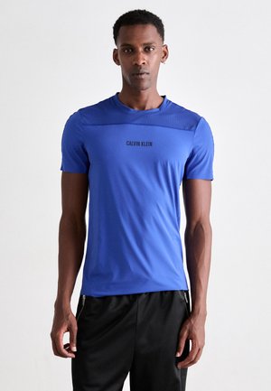 Sininen lyhythihainen urheilupaita, jossa on verkkopaneeli hartioiden alueella ja musta "CALVIN KLEIN" -logo keskellä.