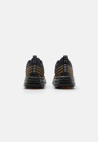 Chaussures de sport noires avec des accents jaunes et une semelle en caoutchouc texturée, dotées d'un design arrière unique et de détails réfléchissants sur le talon.