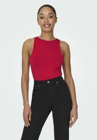 Röd ärmlös topp av mjukt tyg, kombinerad med högmidjade svarta jeans. Enkel design utan synliga mönster eller hårdvarudetaljer.