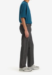 T-shirt teal a maniche corte abbinato a jeans dritti grigio scuro e sneakers sportive grigie, con un taglio pulito e contemporaneo.