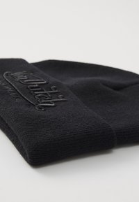 Gorro de punto negro con puño doblado, que presenta un logo en relieve en la parte frontal. La textura es suave y lisa, adecuada para el clima frío.