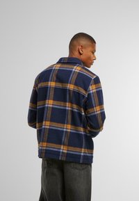 Marine rutete skjorte i flanellstoff med oransje, gule og blå mønstre; har krage og avslappet passform.