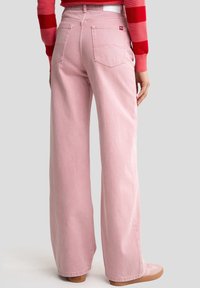 Růžové džínové kalhoty s širokými nohavicemi mají vysoký pas, velké zadní kapsy s charakteristickým prošíváním a hladkou, měkkou texturu.