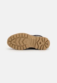 Chaussure de randonnée noire avec une semelle en caoutchouc robuste. La semelle extérieure texturée présente de profondes rainures et une couleur beige, offrant une adhérence sur des terrains variés.