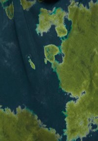 Tekstiili, jossa on tummansininen pohja ja vihreitä tie-dye -kuvioita, jotka muodostavat epäsäännöllisiä muotoja, ja pehmeä, teksturoitu pinta.