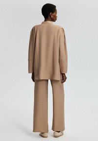 Beige cropped jacket and wide-leg pants in textured fabric. Features a collared neck, long sleeves, and relaxed fit. Pair worn with sneakers.