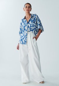 Blue patterned button-up shirt with white abstract designs, paired with loose white trousers featuring an elastic waistband and drawstring.