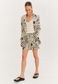 Sako a šortky s květinovým vzorem v černých a béžových tónech, doplněné béžovým topem a černými sandály.