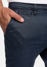 Marineblaue Hosen aus glattem Stoff, mit einer dezenten Textur, seitlichen Taschen und einem frontalen Knopfverschluss.