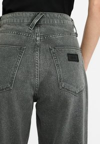 Jeans in denim grigio a vita alta con una leggera scintilla. Presenta due tasche posteriori e un'etichetta nera con logo in vita. Finitura testurizzata.