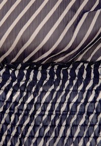 Tessuto a righe blu navy e bianche con una texture trasparente e plissettata, dotato di una vita arricciata e cuciture delicate lungo il bordo superiore.