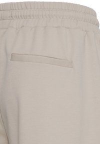 Pantalon à taille élastique beige clair avec une poche arrière horizontale unique sans détails de fermeture visibles.