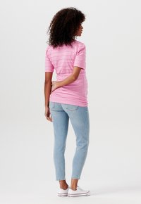 Růžový texturovaný top s vodorovnými pruhy, doplněný světlými modrými úzkými džíny a bílými teniskami. Pohled zezadu ukazuje přiléhavý střih.