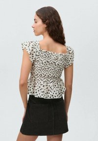 Blouse blanche avec imprimé animal noir, corsage smocké et manches volantées, associée à une jupe en denim noire avec deux poches arrière.