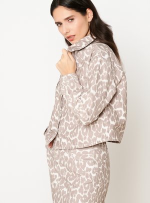 Krátka bunda z béžovej látky s bielym leopardím vzorom, so stojáčikovým golierom a zapínaním na gombíky, kombinovaná s nohavicami v rovnakom štýle.