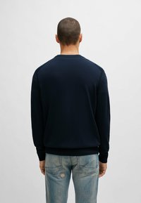 Marineblauwe gebreide trui met lange mouwen, geribbelde manchetten en zoom, ronde halslijn en een gladde textuur. Gedragen over lichtgewassen versleten jeans.