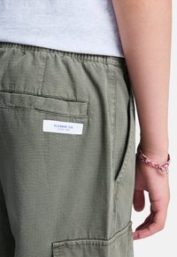 Olivgrüne Shorts aus leichtem Material mit einem strukturierten Muster, Seitentaschen und einem weißen Etikett mit "ELEMENT CO."