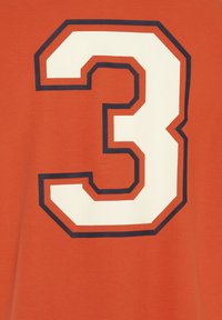 Oranger Stoff mit einer großen, strukturierten, weißen Zahl "3", die von marineblau umrandet ist. Das Design ist auffällig und zentriert auf dem Kleidungsstück.