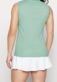 Sportovní tílko bez rukávů ze světle zelené látky, s bílou rozšířenou sukní dole a malým logem na zádech.